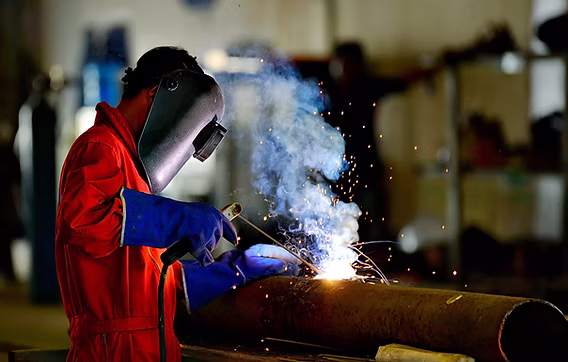 Peserta mengikuti pelatihan teknik pengelasan menggunakan helm las dan sarung tangan saat menyambungkan logam.